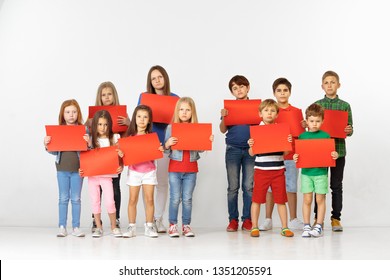 Group of sad serious angry children with red empty banners isolated on studio background. Education and advertising concept. Protest and children's rights concepts.