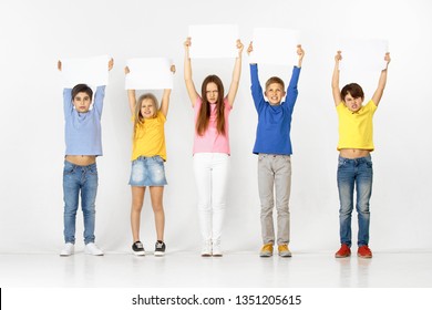 Group of sad serious angry children with a white empty banners isolated in white studio background. Education and advertising concept. Protest and children's rights concepts.