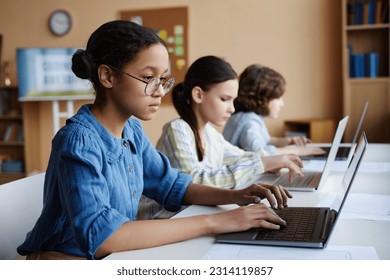 Group of school children studying with computers while sitting at table in class - Powered by Shutterstock