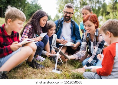 Group Of School Children With Teacher And Windmill Model On Field Trip In Nature.