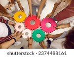 Group of school, college or university students working on project all together. Team of young people holding colorful green, pink, red, yellow gear cog wheels. Top view. Education, teamwork concept