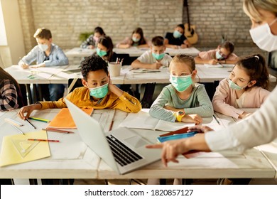 Group of school kids with protective face masks learning on laptop with their teacher during a class in the classroom.  - Powered by Shutterstock