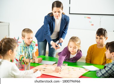 Group Of School Kids With Teacher Sitting Together Around Desk In Classroom, Playing Educational Tabletop Game