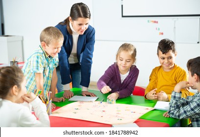 Group Of School Kids With Teacher Sitting Together Around Desk In Classroom, Playing Educational Tabletop Game