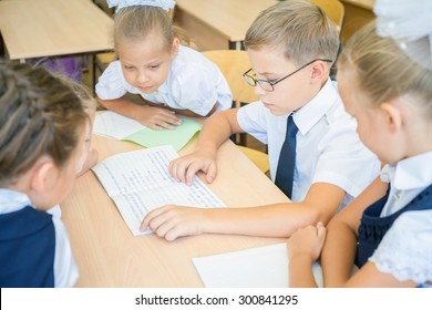Group of schoolchildren or kids at school classroom sitting at a desk and help each other with their homework. Concept of teamwork among students