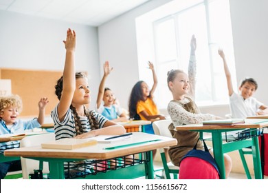group of schoolchildren raising hands to answer question during lesson