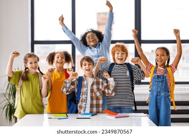 Group of schoolchildren and teacher standing together, celebrate   successful completion of collective school work and   raising their hand in class during lesson - Powered by Shutterstock