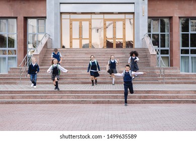 Group Of Schoolchildren In Uniform Are Running Down The Stairs Out Of School.