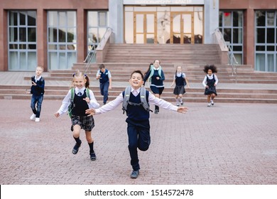 Group Of Schoolchildren In Uniform Are Running Down The Stairs Out Of School.