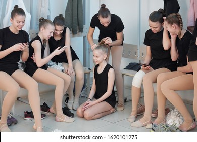 Group of schoolgirls preparing for cheerleading training in locker room: girls using smartphones for surfing net while brunette girl making ponytail to friend - Powered by Shutterstock