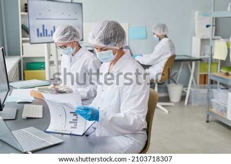Group of scientists sitting at the table and working with statistics during pandemic in the laboratory