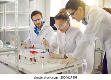 Group of scientists working in science laboratory. Pharma chemists or biotech company employees in lab coats and goggles preparing to conduct experiment and transferring sample liquid on Petri dish - Powered by Shutterstock