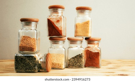 A group of seasonings in glass jars on a light wooden background. Paprika, herbs, mustard, garlic, front view, selective focus - Shutterstock ID 2394916273