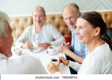 Group Of Senior Companions Sitting By Table In Cafe And Having Talk By Cup Of Coffee