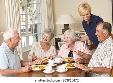 Group Of Senior Couples Enjoying Meal Together In Care Home With Home Help