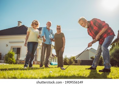 Group Of Senior Friends Having Fun Playing Mini Golf At The Backyard Lawn, Spending Sunny Summer Day Outdoors