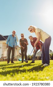 Group Of Senior Friends Having Fun Playing Mini Golf At The Backyard Lawn, Spending Sunny Summer Day Outdoors