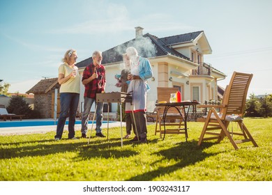 Group of senior friends having a poolside backyard barbecue party, gathered around the grill, grilling meat and having fun spending sunny summer day outdoors