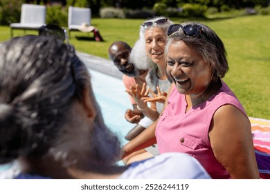 Group of senior friends laughing and relaxing by pool on sunny day. Friendship, leisure, summer, relaxation, fun, outdoors, poolside, vacation, unaltered - Powered by Shutterstock