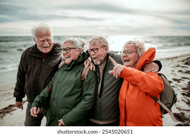 Group of senior friends laughing together on windy beach in raincoats - Powered by Shutterstock