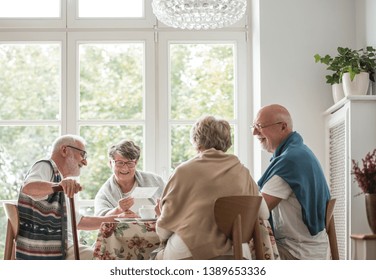 Group Of Senior Friends Sitting Together At The Table At Nursing Home Dining Room