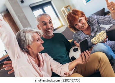 Group Of Senior Friends Support Favorite Sports Team Together Use Smartphone App To Online Bet