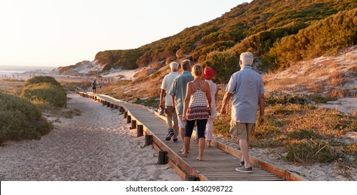 Group Of Senior Friends Walking Along Boardwalk At Beach On Summer Group Vacation