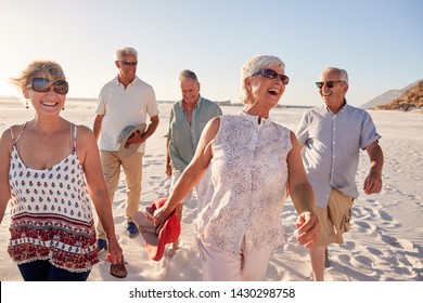 Group Of Senior Friends Walking Along Sandy Beach On Summer Group Vacation