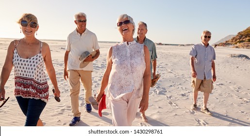 Group Of Senior Friends Walking Along Sandy Beach On Summer Group Vacation - Powered by Shutterstock