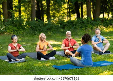 Group of senior people attending yoga class with instructor outdoors, older men and women sitting on mats in lotus position, practicing meditation, enjoying training outside, copy space - Powered by Shutterstock