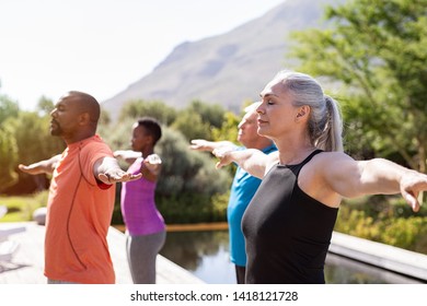 Group of senior people with closed eyes stretching arms outdoor. Mature yoga class doing breathing exercise. Women and men doing breath exercise with outstretched arms. Balance and meditation concept.