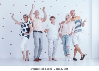 Group of senior people dancing together during a birthday party in bright room with gold dots wallpaper