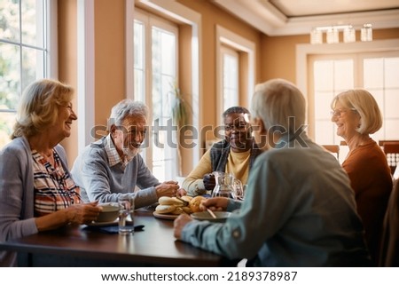 Group of senior people enjoying in conversation during lunch at dining table at nursing home. 