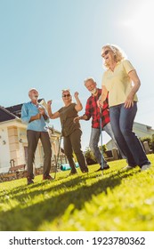 Group Of Senior People Having Fun Playing Mini Golf At The Backyard Lawn On A Sunny Summer Day