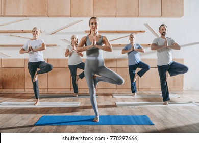 Group Of Senior People Practicing Yoga With Instructor In Tree Pose On Mats In Studio