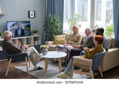 Group Of Senior People Resting On Sofa In The Living Room And Watching News On TV Together