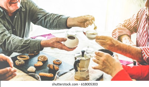 Group of senior people toasting italian style moka coffee after lunch - Mature happy friends eating biscuits and laughing together - Focus on men bottom hands - Warm contrast cine filter - Powered by Shutterstock