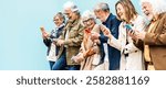 Group of senior people using technology devices together standing on a blue wall - Happy older friends having fun watching funny video on smartphone - Tech and modern elderly concept