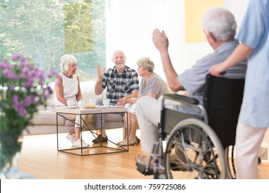 Group Of Senior People Welcoming A Friend While Sitting Together In Living Room