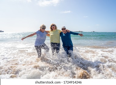 Group Of Senior Retired Women On Their 60s And 70s Falling In The Water Having Fun On The Beach. Older Ladies Laughing As They Fall Down Loosing Balance. Humor Senior Health And Aging Together.