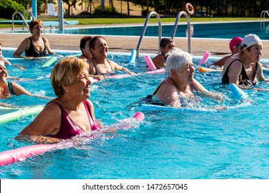 Group of senior women in action doing aqua gym with foam noodles in outdoor swimming pool.