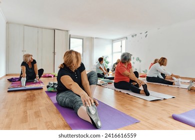 A group of senior women engage in various yoga exercises, including neck, back, and leg stretches, under the guidance of a trainer in a sunlit space, promoting well-being and harmony - Powered by Shutterstock