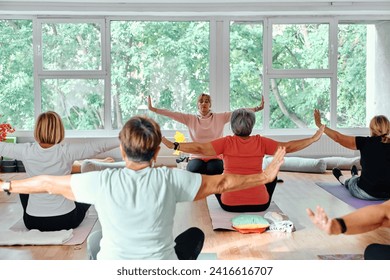 A group of senior women engage in various yoga exercises, including neck, back, and leg stretches, under the guidance of a trainer in a sunlit space, promoting well-being and harmony - Powered by Shutterstock