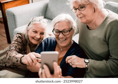 Group of senior women laughing at smartphone together in home living room - Powered by Shutterstock