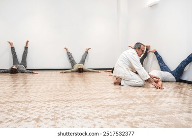 A group of senior women practice the legs-up-the-wall yoga pose while their instructor helps adjust postures. Concept of guided yoga for flexibility and relaxation. - Powered by Shutterstock