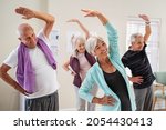 Group of seniors doing stretching exercise together at retirement centre. Elderly men and old women exercising at nursing home during daily fitness. Retired couples exercising at care facility.