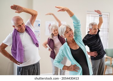 Group of seniors doing stretching exercise together at retirement centre. Elderly men and old women exercising at nursing home during daily fitness. Retired couples exercising at care facility.