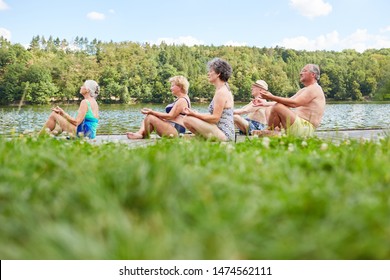 Group Of Seniors Doing Yoga Exercises On The Lake In Summer