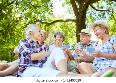 Group Of Seniors Friends Play Cards Together In The Summer In The Garden