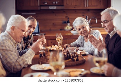 Group of seniors friends playing chess while having dinner and wine in the dining room at home - Powered by Shutterstock